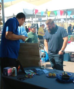Jason hood pointing out different engraved signs on the display to a potential customer at the Tempe Trophy booth.