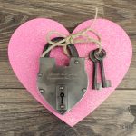 Engraved silver hand-forged love lock on top of a pink heart